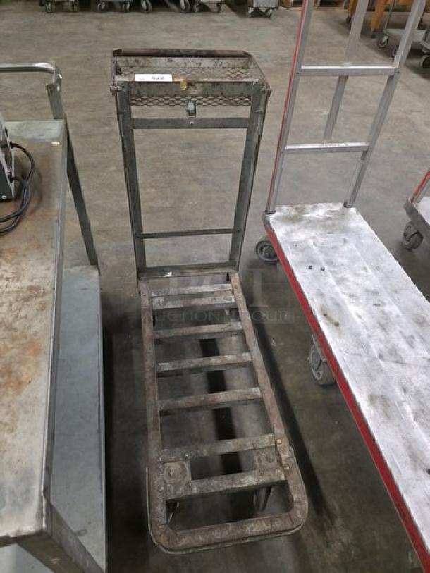 Metal utility cart on wheels, features grid platform, upright handle, used condition, suitable for warehouse tasks.
