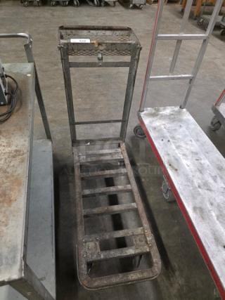 Metal utility cart on wheels, features grid platform, upright handle, used condition, suitable for warehouse tasks.