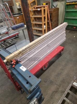 Lot of pallet rack beams stacked on a red dolly in a warehouse. Metal beams show markings and wear, indicating heavy use.