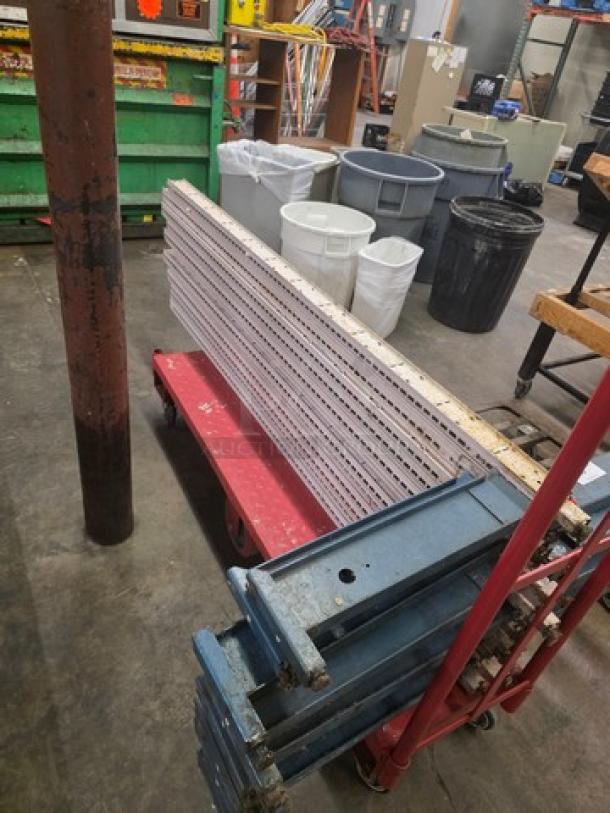 Lot of pallet rack beams on a red cart in a warehouse setting. Beams are metal, well-structured, and stackable.