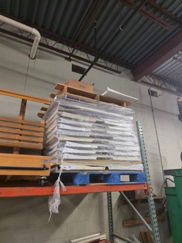 Pallet of gondola shelving parts, wrapped in plastic, mixed sizes and materials, used condition, stacked on a blue pallet.