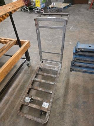 Utility cart with metal frame and handle, visible wear, four wheels, and open platform design; ideal for heavy-duty transport.