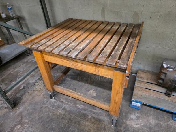 Wooden display stand with slatted top, caster wheels, and sturdy frame. Visible wear. Ideal for retail or exhibition use.