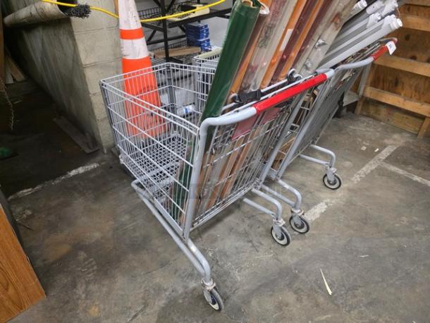 Lot of two metal shopping carts with black and red handles, in used condition, containing various items.