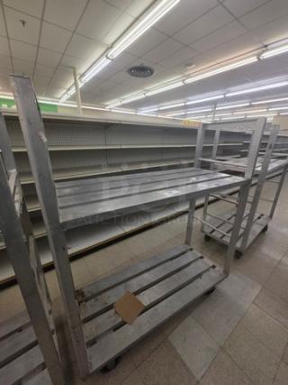 Aluminum mobile shelf cart with three slatted shelves on wheels. Used condition with visible wear marks. Store setting.