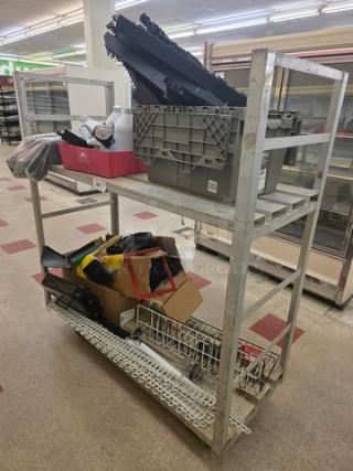 Aluminum mobile cart with three shelves, used condition, visible wear, cluttered with various items. Ideal for storage or transport.