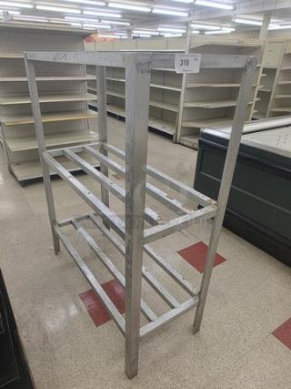 Metal dunnage rack with three slatted shelves, showing wear. Auction tag number 310. Used for storage in commercial settings.