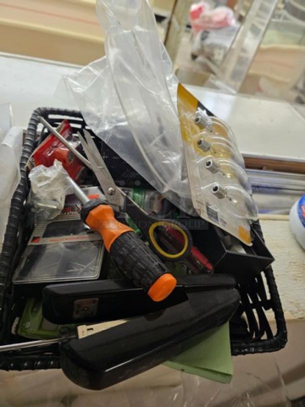 A basket of miscellaneous small items including tools, stapler, and packaged hardware, suitable for various uses.