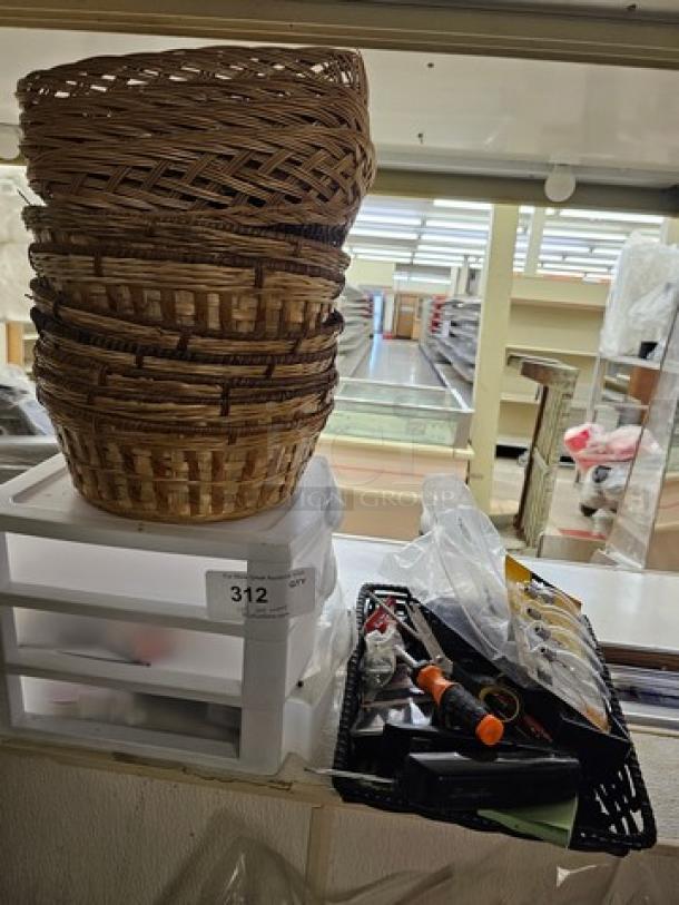 A stack of wicker baskets atop a plastic organizer, next to a tray of miscellaneous small items including tools, in used condition.