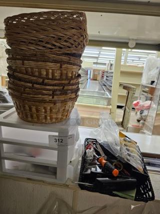 A stack of wicker baskets atop a plastic organizer, next to a tray of miscellaneous small items including tools, in used condition.
