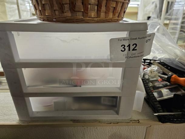 Lot of miscellaneous small items, including a wicker basket on top of a plastic drawer unit. Label marked "312."
