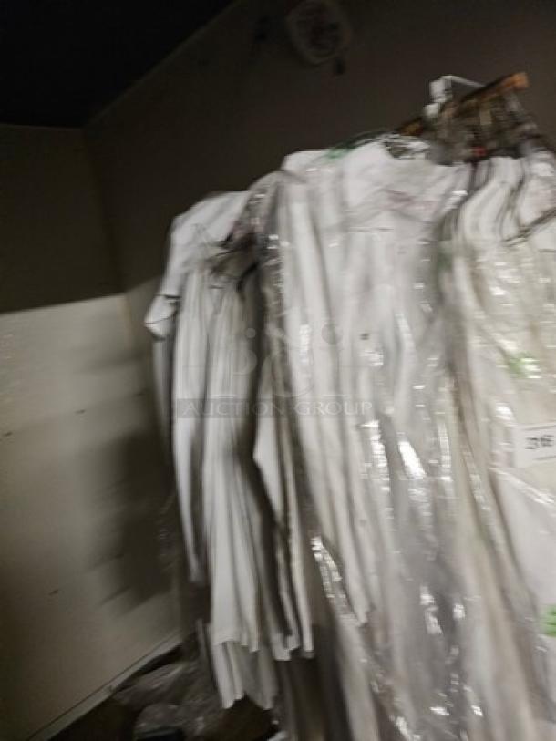 Lot of white butcher coats, hung on a rack, covered in transparent plastic. Appears in good condition.