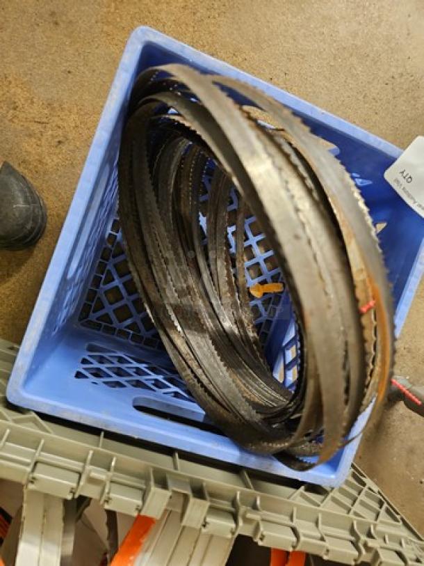 Lot of band saw blades in a blue crate, various lengths and teeth configurations, used condition, ideal for metal or wood cutting.