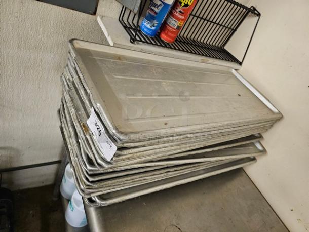 Lot of 30 commercial baking sheets, silver, used condition, stacked on metal surface. Tag reads "30XBID."