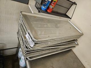 Lot of 30 commercial baking sheets, silver, used condition, stacked on metal surface. Tag reads "30XBID."