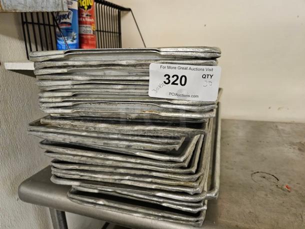 Lot of 30 commercial baking sheets with visible wear, stackable design. Tag indicates quantity and auction info: "320, QTY 30, PCIAuctions.com."