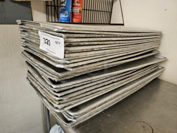 Lot of 30 commercial baking sheets stacked on a metal surface, showing signs of use, with a label indicating quantity.