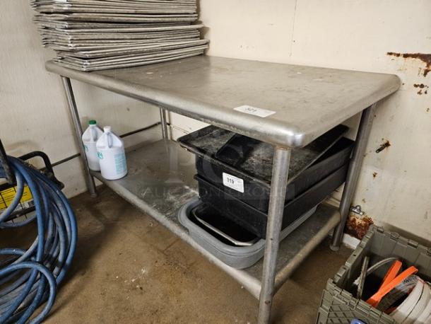 Stainless steel work table with two-tier design, showing surface wear. Contents not included. Has a smooth tabletop and sturdy legs.