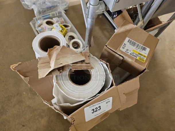 Box containing rolls of white plastic sheeting, showing labels with lot number 323 and packaging details.