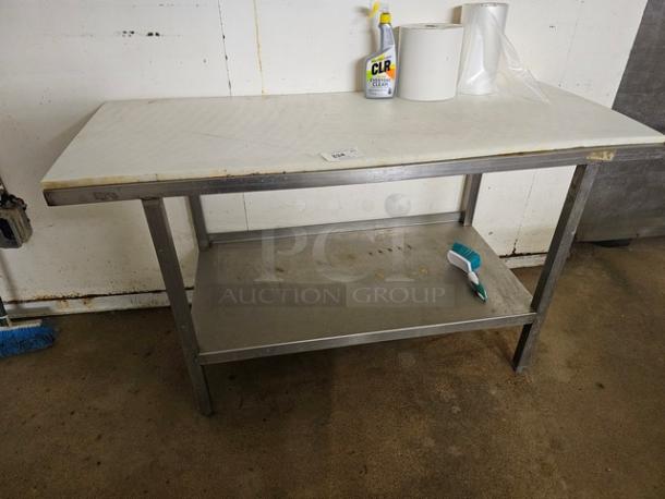 Stainless steel butcher block table with white cutting board top, lower storage shelf, and fair condition. Cleaning supplies on top.