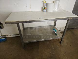 Stainless steel butcher block table with white cutting board top, lower storage shelf, and fair condition. Cleaning supplies on top.