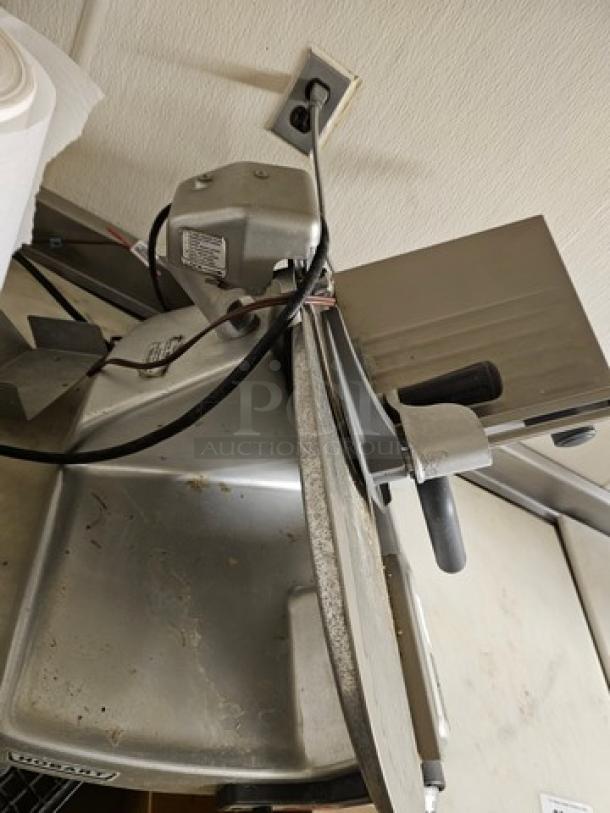 Hobart slicer, metal build, used condition with visible wear. Equipped with a sharp blade and adjustment knob. Model tag present.