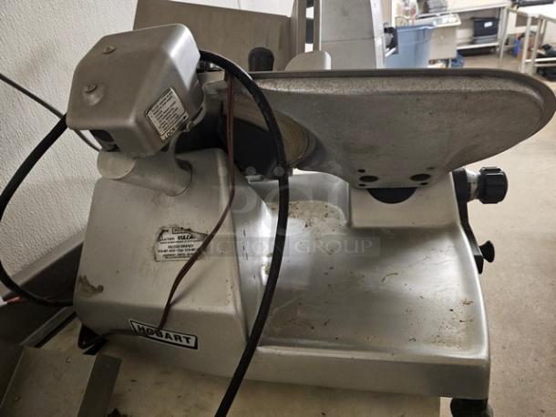 Hobart slicer, metal construction, used condition with visible wear. Features a motor housing and adjustable slicing arm. Model labels intact.