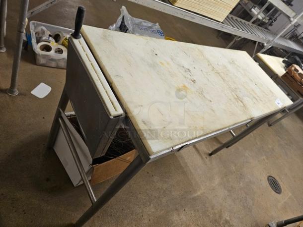 Cutting board butcher block table with metal legs, showing wear on the surface. Equipped with knife slots and storage shelf.