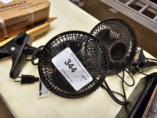 Two small black clip-on fans with mesh guards and power cords, in used condition. Auction tag marked "344" visible.