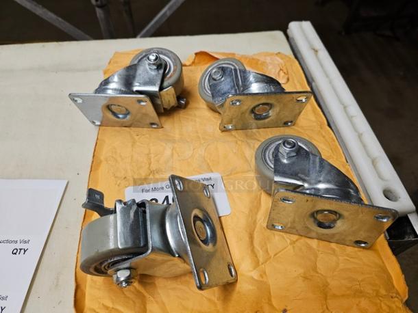 Lot of four metal swivel casters on a table, with mounting plates, in good condition, resting on a paper envelope.
