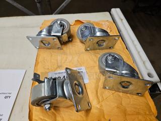 Lot of four metal swivel casters on a table, with mounting plates, in good condition, resting on a paper envelope.