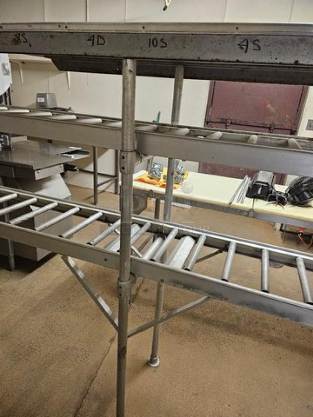 Stainless steel roller conveyor system in good condition, featuring multiple rollers and sturdy frame. Markings include "8S," "4D," "10S," "4S."