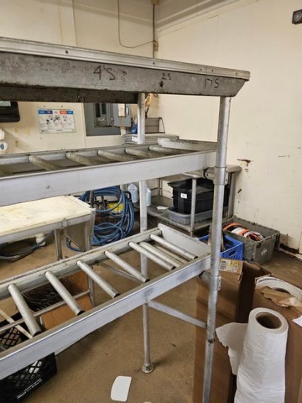 Stainless steel roller conveyor system in used condition, featuring multiple rollers and marked with numbers. Buyer handles removal.