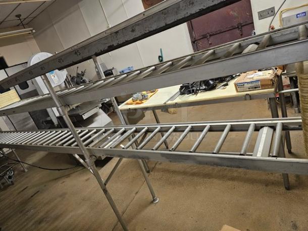 Stainless steel roller conveyor system, industrial-grade, sturdy frame. Visible wear and label markings for length. Buyer responsible for removal.