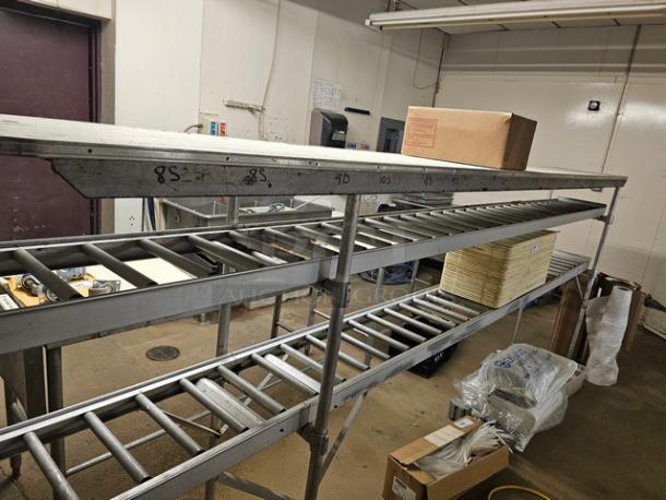 Stainless steel roller conveyor system in industrial setting, used condition. Markings include measurements like "85" and "4D".