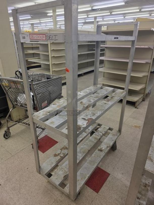 Aluminum mobile shelf cart, four tiers, worn condition, caster wheels, "Deli Cooler" label, ideal for storage or transport.