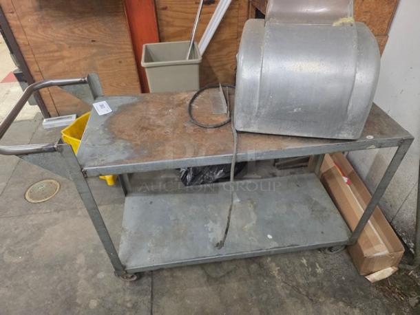 Industrial utility cart with two shelves, metal frame, and handle. Top surface shows wear. Contents not included.