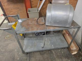 Industrial utility cart with two shelves, metal frame, and handle. Top surface shows wear. Contents not included.