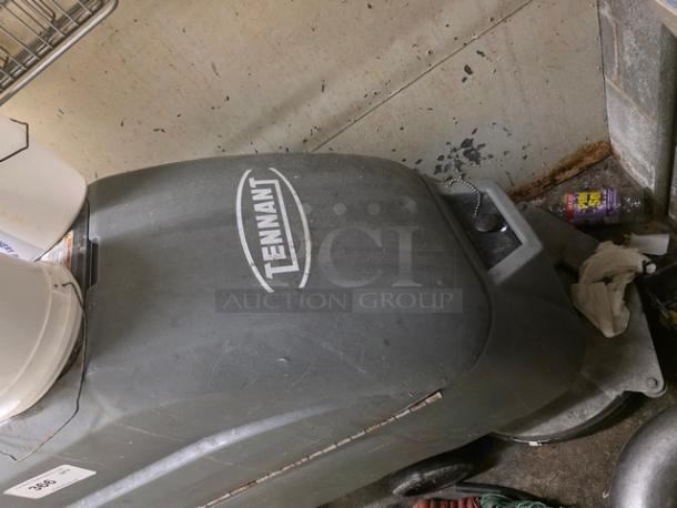 Tennant floor scrubber in used condition. Features visible wear and Tennant branding on the body. Suitable for industrial cleaning.