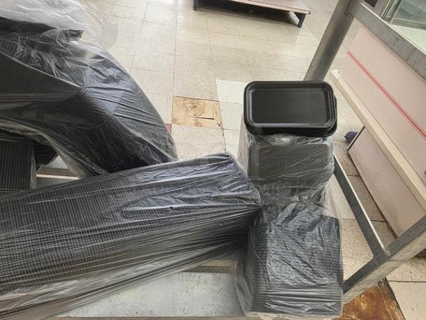 One lot of disposable food trays, black, stacked and wrapped in plastic, suitable for catering use.