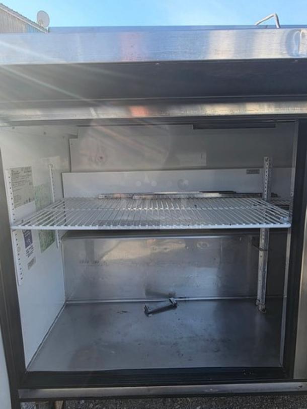 True QA-60-24M-B 60" refrigerated prep table, stainless steel, open door, showing interior shelving and storage space.