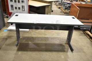 Gray desk with a sleek design, featuring two cable management grommets. Slightly worn surface, ideal for office use.