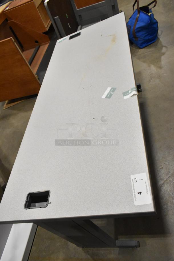 Gray desk with metal frame, rectangular shape, multiple surface marks. Cutout holes for cable management. Auction label visible.