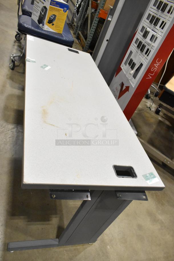 Gray desk with rectangular top, cable management holes, and adjustable metal legs. Noticeable surface marks. Good condition.