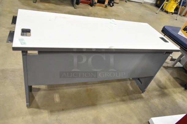 Gray desk with white top, rectangular shape, metal frame, minor wear visible, cable cutouts, modern design.