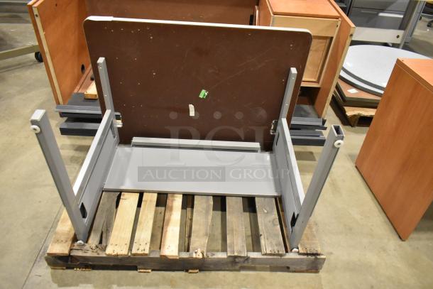 Gray desk with metal frame and wood desktop, partially assembled on a pallet. Visible scratches, moderate wear.