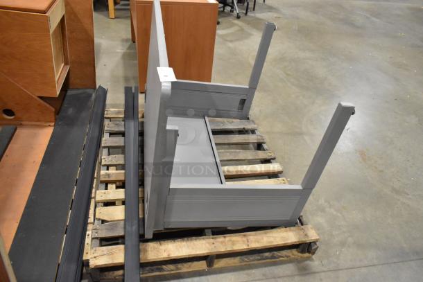 Gray desk frame on a pallet, disassembled. Made of sturdy material, unmarked condition. Suitable for office setup.