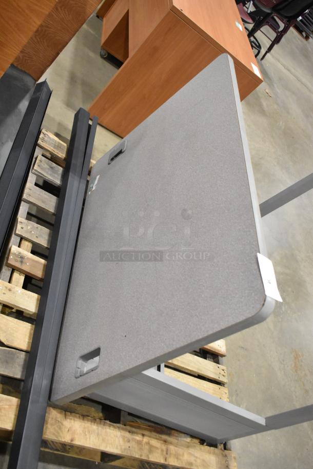 Gray desk on pallet, showing a smooth surface and integrated cable management cutout. Appears in good condition.
