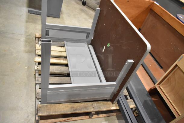 Gray desk in good condition, shown disassembled on a wooden pallet. Features sturdy metal frame and tabletop.
