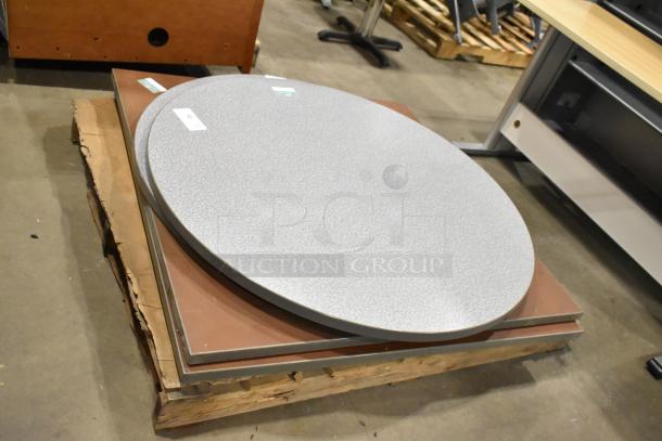 Five tabletops, various shapes and colors, including round and square. Each tabletop is stacked and labeled for bidding.